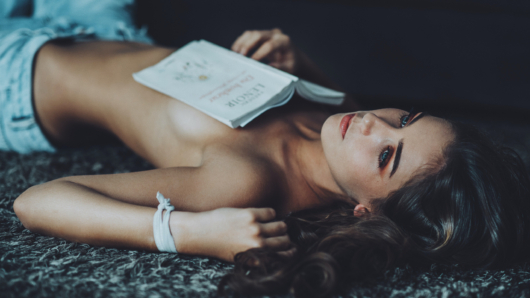topless woman lying on ground while holding white book